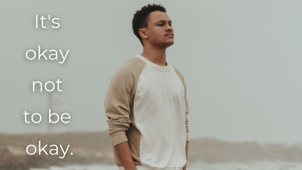 Man standing with his eyes closed and hands in his pockets with text "It's okay not to be okay."