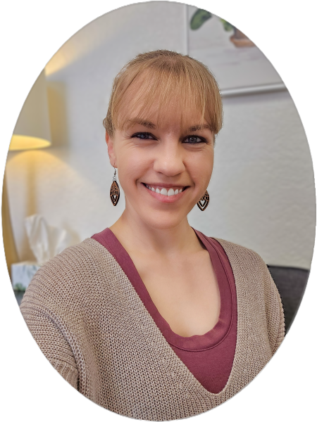 Smiling blond woman wearing a pink shirt and brown sweater with a lamp behind her
