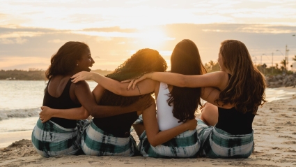 Dauntless Counseling Anxiety Therapy for Women - Image of 4 women sitting on a beach laughing with their arms around each others shoulders