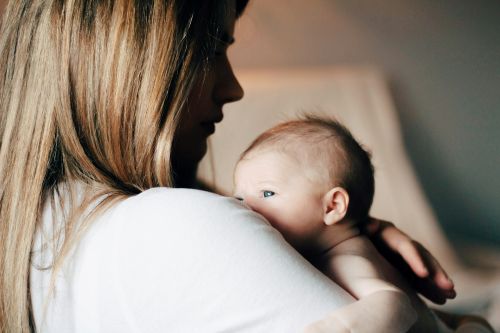Woman with blond hair and her face shadowed holding a small baby with blue eyes